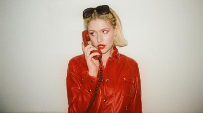 Yeva in einer auffälligen Roten Jacke hält ein rotes Kabeltelefon an ihr Ohr.
