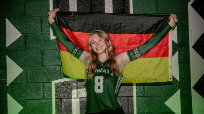 Paula hält die Deutschlandflagge gespannt über ihrem Kopf und steht vor dem Hawaii University Zeichen