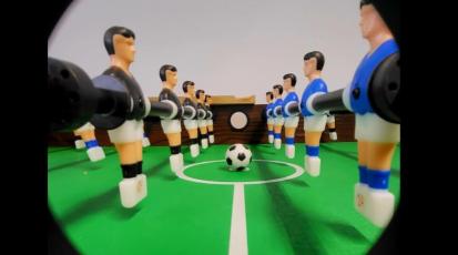 Ein Fußball liegt auf dem Anstoßkreis eines Tischkickers zwischen zwei Spielern.