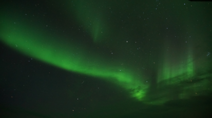 Auf dem Foto ist ein dunkler Himmel und ein grünes Polarlicht zu sehen.