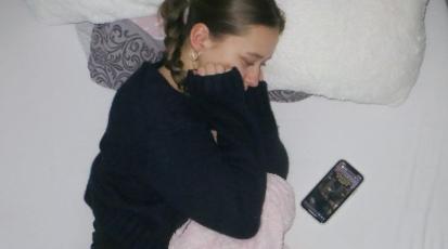 Trauriges Mädchen auf dem Bett schaut auf ihr Handy.