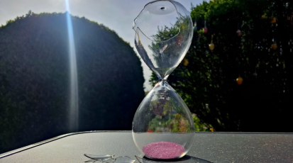 Eine kaputte Sanduhr auf einem Tisch in der Natur.