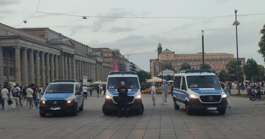 Ein Polizist steht mittig vor drei Polizeiwägen