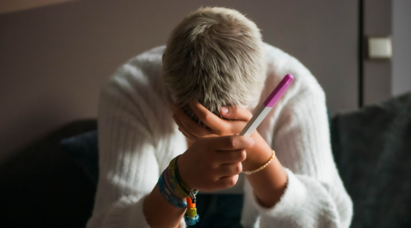 Frau am Weinen hält Schwangerschaftstest in der Hand.