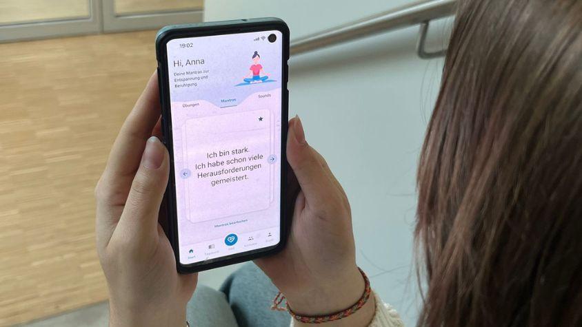 Eine Studentin hält ihr Handy, auf dem eine Seite der App zu sehen ist.