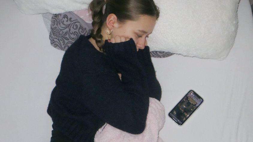 Trauriges Mädchen liegt auf dem Bett und schaut aufs Handy.