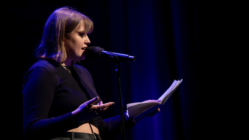 Auf der Bühne, mit dem Mikro vor sich und ihrem eigenen Text in der Hand, steht Evelyn beim Poetry Slam