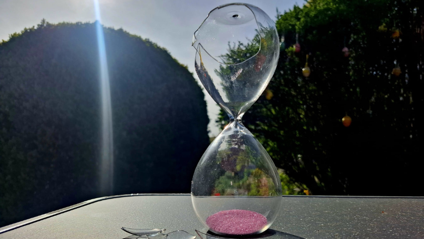 Eine kaputte Sanduhr neben Scherben auf einem Tisch.