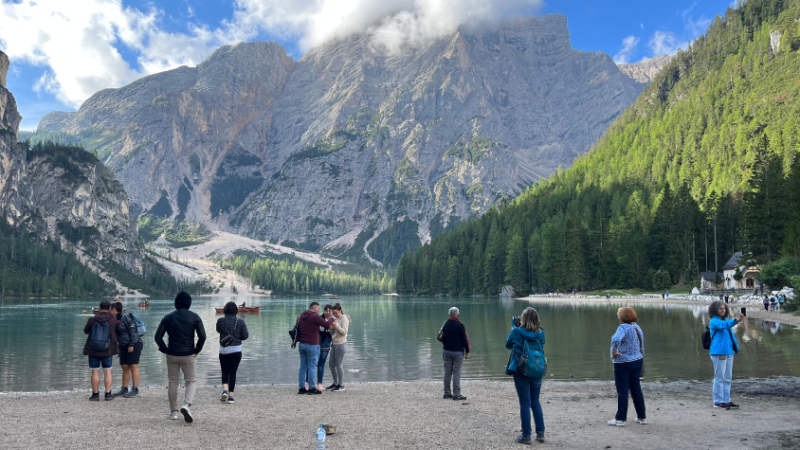 See und Berg im Hintergrund, vor dem See stehen Selfie-machende Tourist*innen.