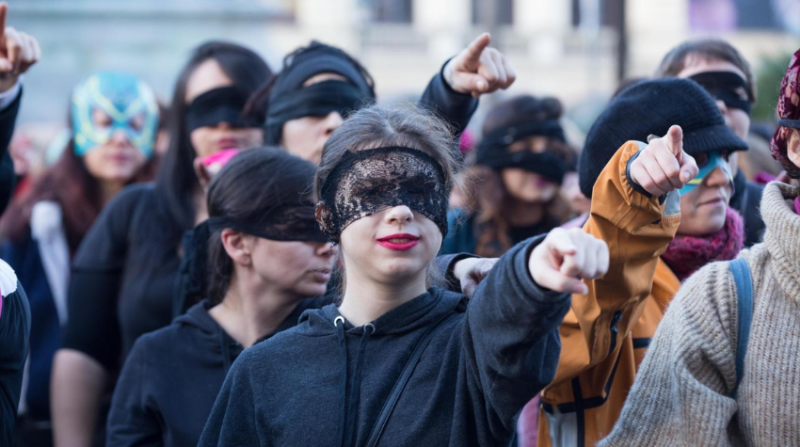 Maskierte Frauen zeigen während einer Protestperformance mit dem Finger 