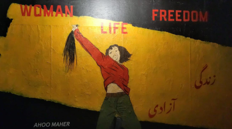 Graffiti einer Frau die einen abgeschnittenen Bündel ihrer Haare in die Luft streckt, darauf die Worte "Woman, Life, Freedom"