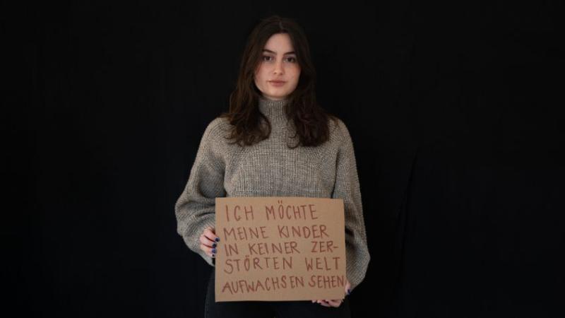 Es ist eine junge Frau mit einem Schild zu sehen. Auf dem Schild steht: Ich möchte meine Kinder in keiner zerstörten Welt aufwachsen sehen. 