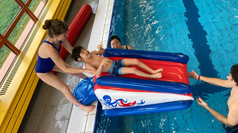 Annette unterstützt einen Jungen mit einer Rutsche ins Wasser zu gehen