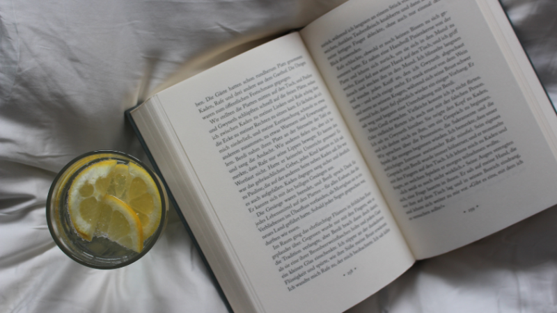 offenes Buch mit einem Wasser daneben, in welchem Zitronenscheiben sind