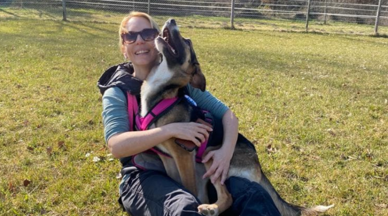 Eine Frau mit ihrem Hund auf einer Wiese. Der Hund schaut glücklich nach oben.